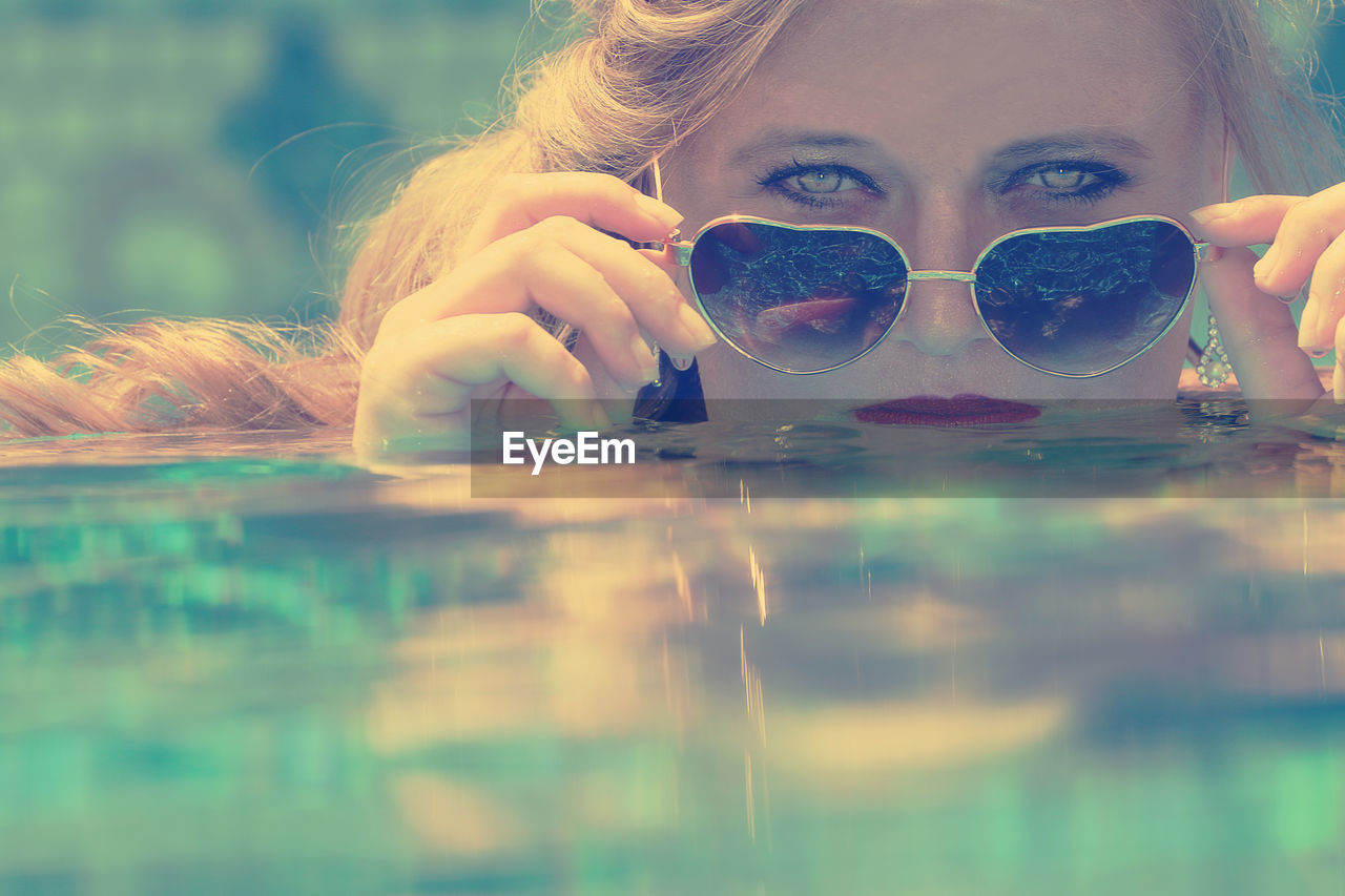 Close-up portrait of woman with sunglasses swimming in water