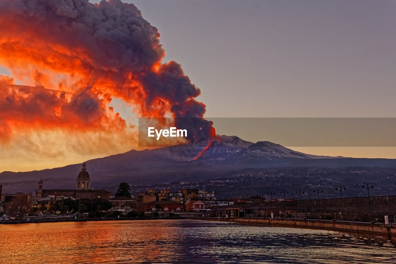 Illuminated buildings in the city during etna eruption