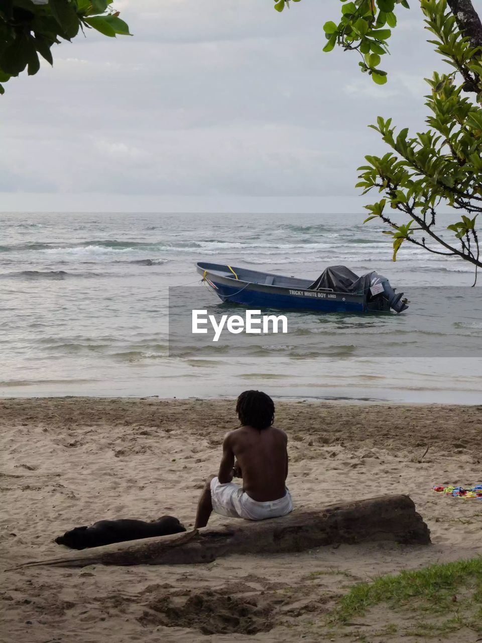 REAR VIEW OF MAN SITTING ON BEACH