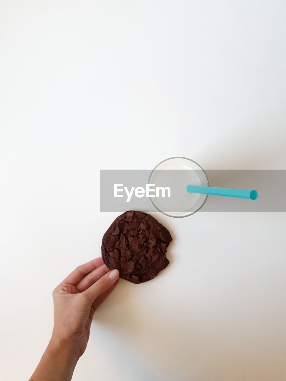 Cropped image of woman holding chocolate cookie by milk in glass on white background