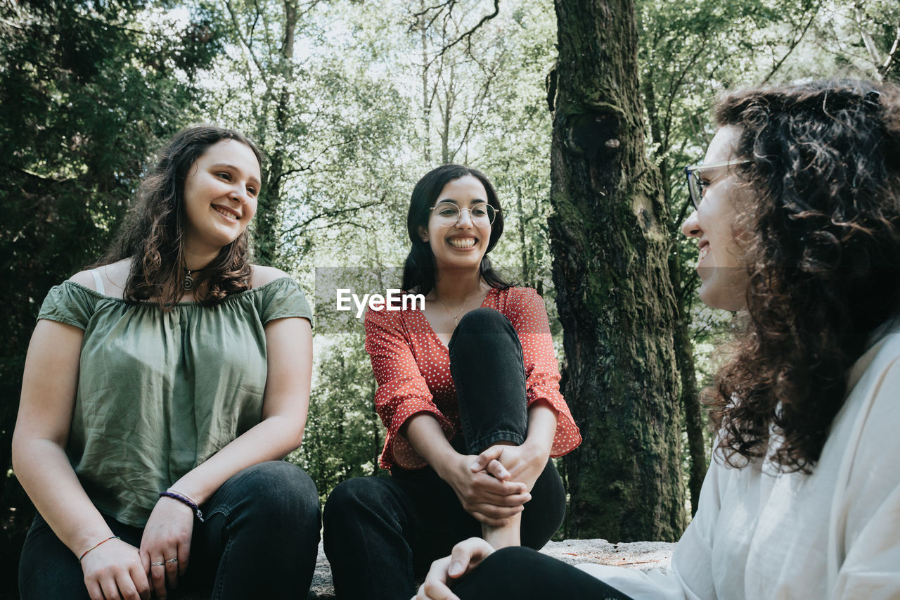 portrait of smiling friends sitting against trees in forest
