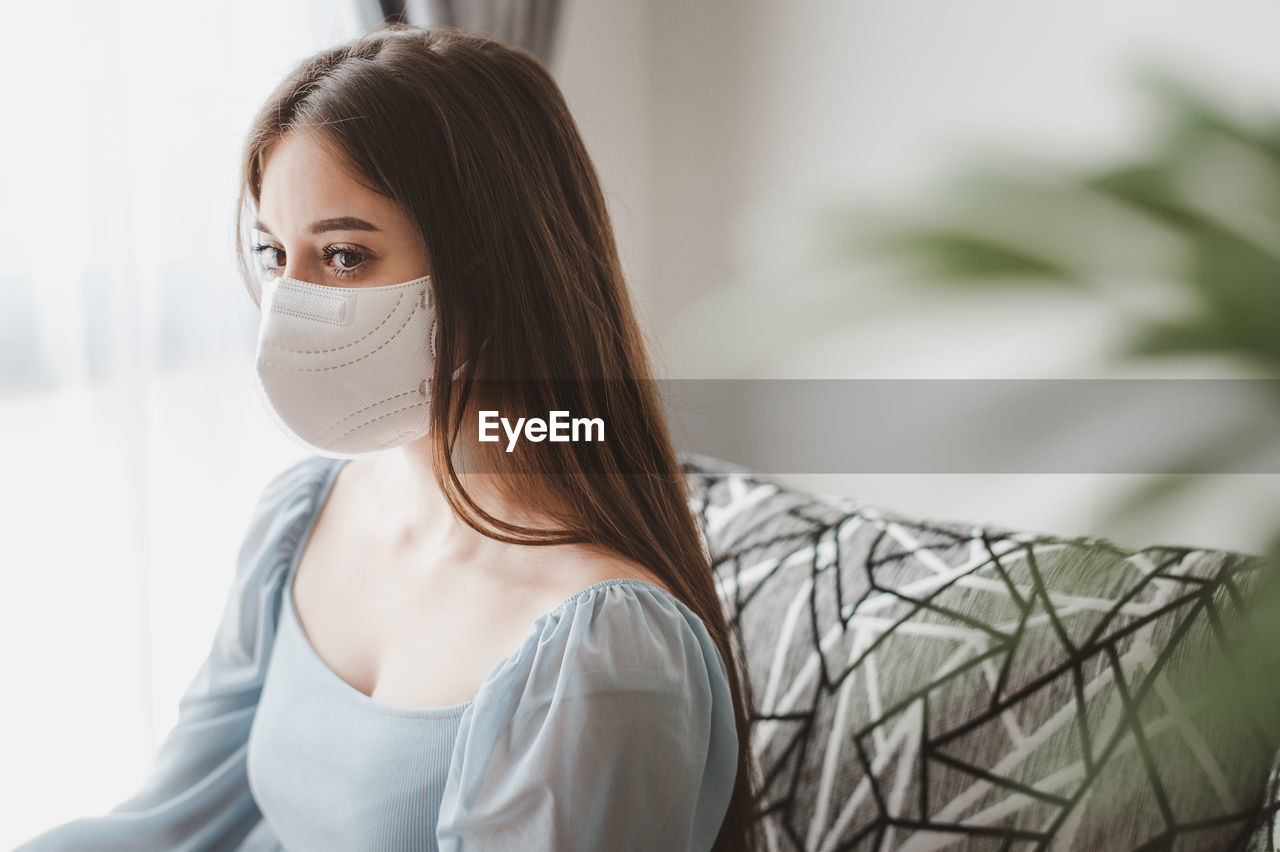 Close-up of young woman wearing mask sitting at home