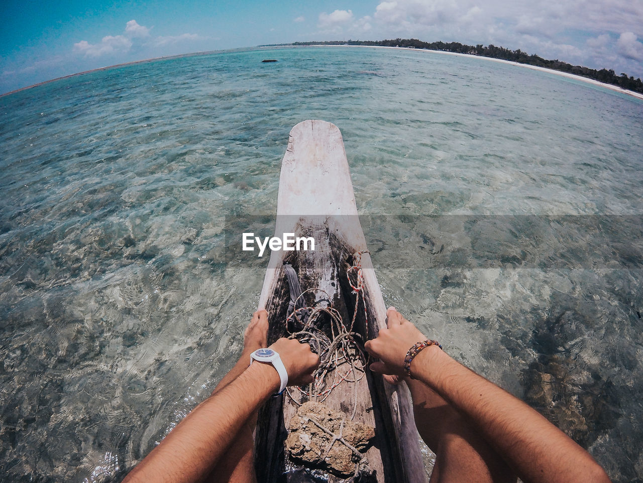 Low section of man sitting on log boat in sea