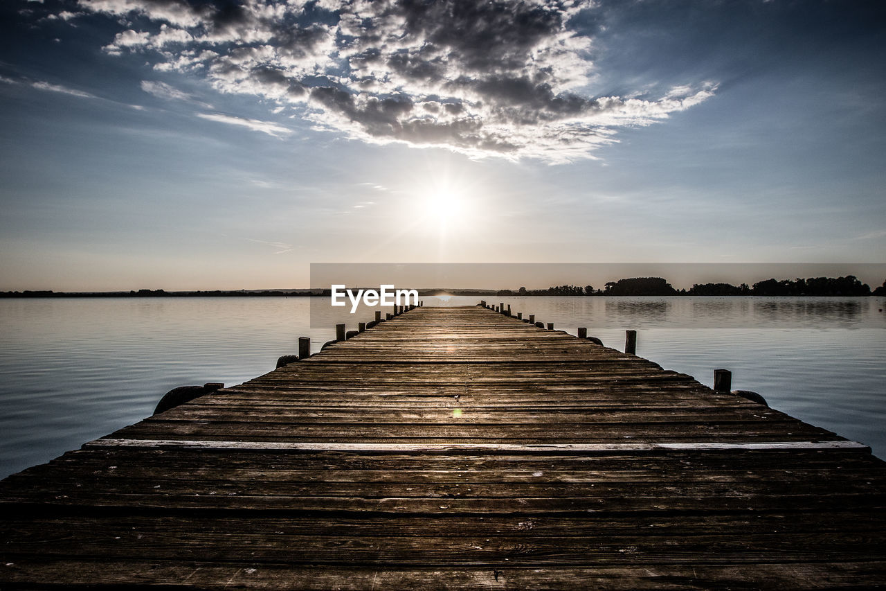 Wooden pier over lake against sky during sunset