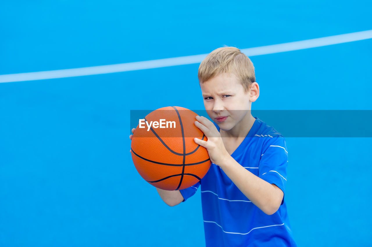 Portrait of boy holding basketball while standing on sports court