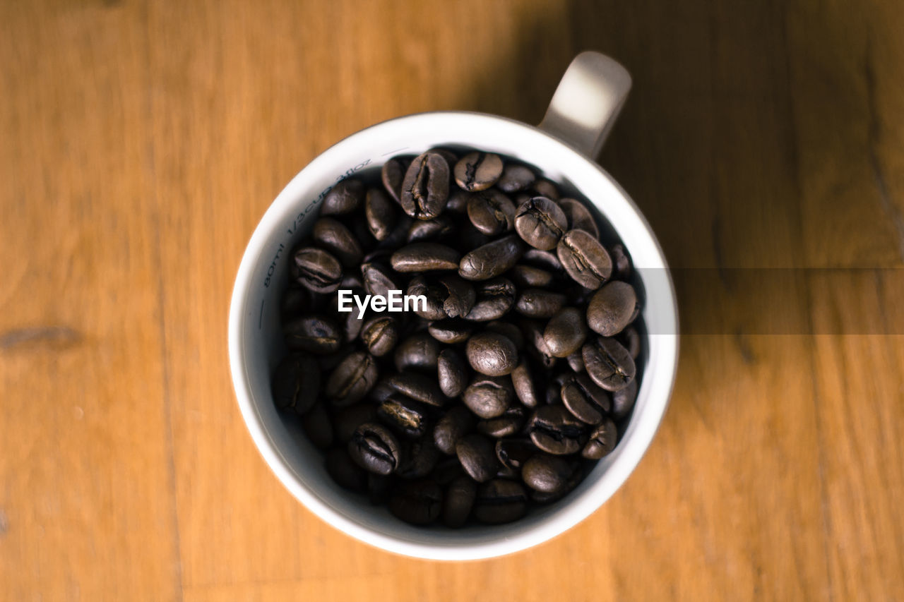 Directly above shot of roasted coffee beans in cup on hardwood floor