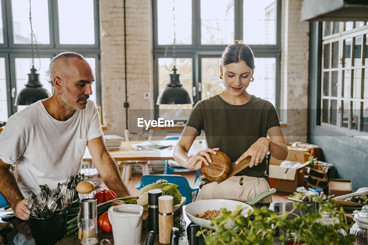 Male colleague looking at female chef preparing food in studio