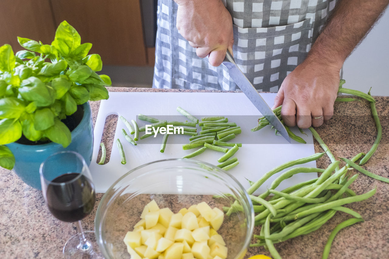 Midsection of man cutting green beans on cutting board in kitchen