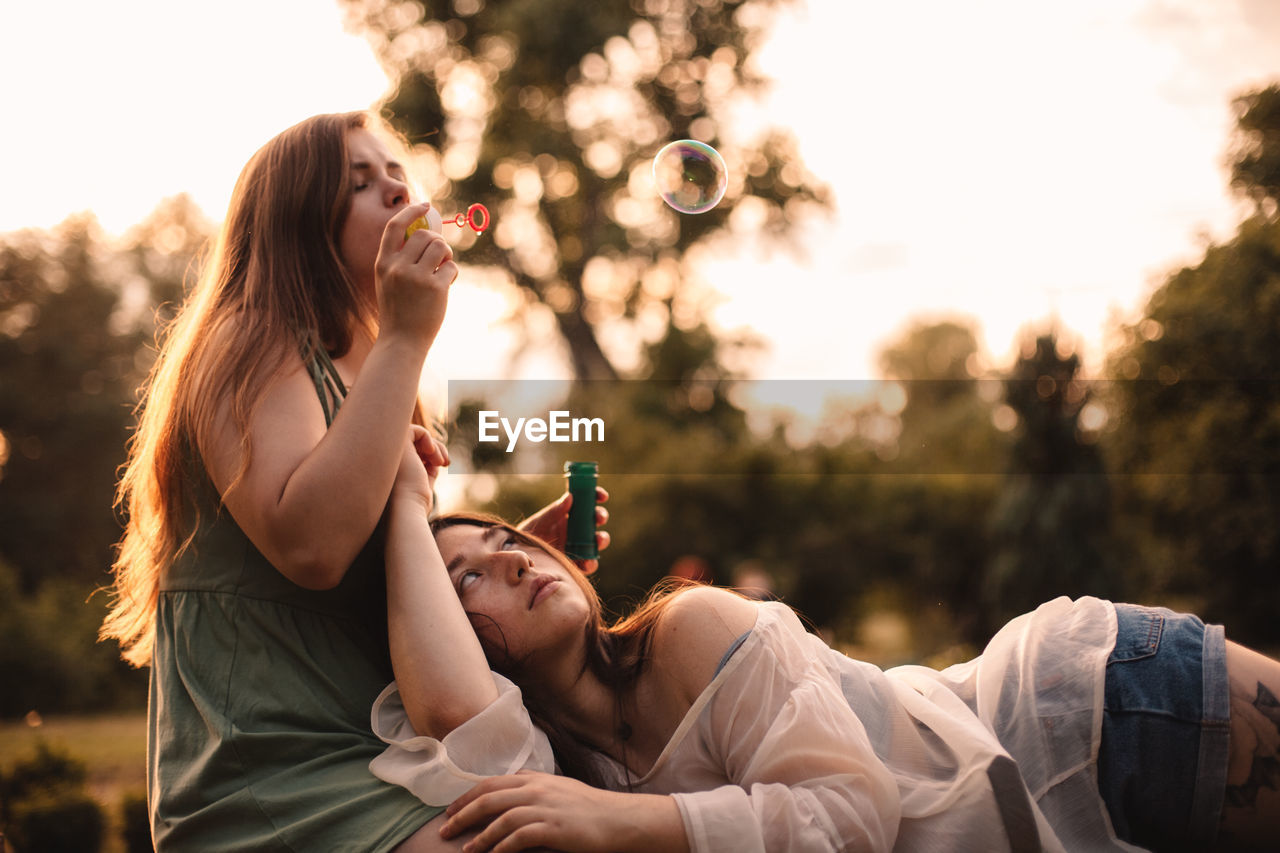 Lesbian couple playing with bubbles while relaxing in park in summer