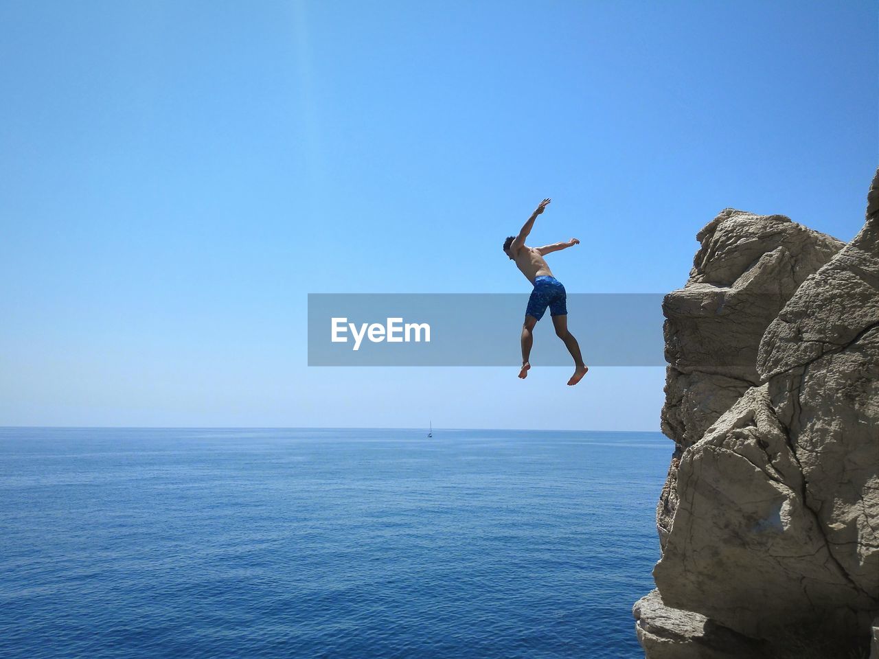 Full length of man jumping in sea against clear blue sky