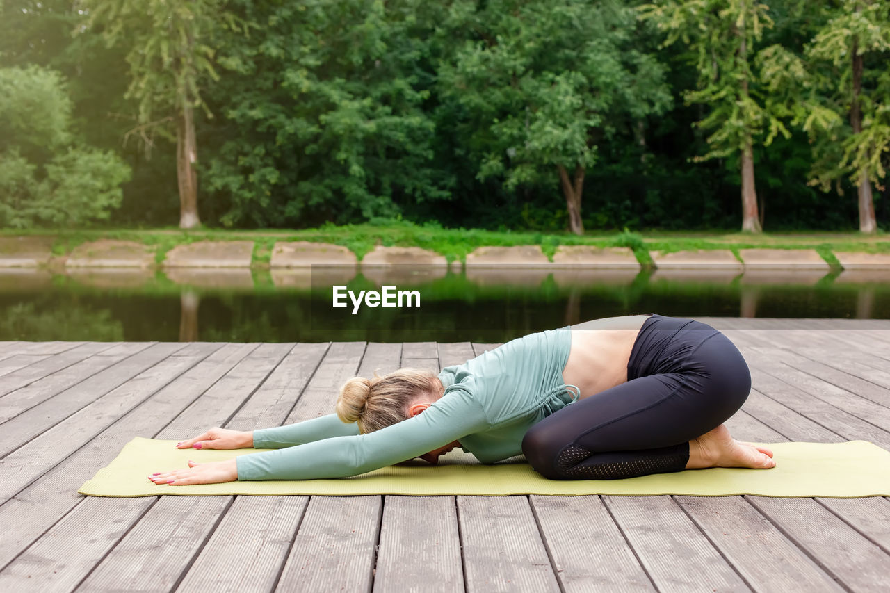 A woman in sportswear on a wooden platform in summer, does yoga