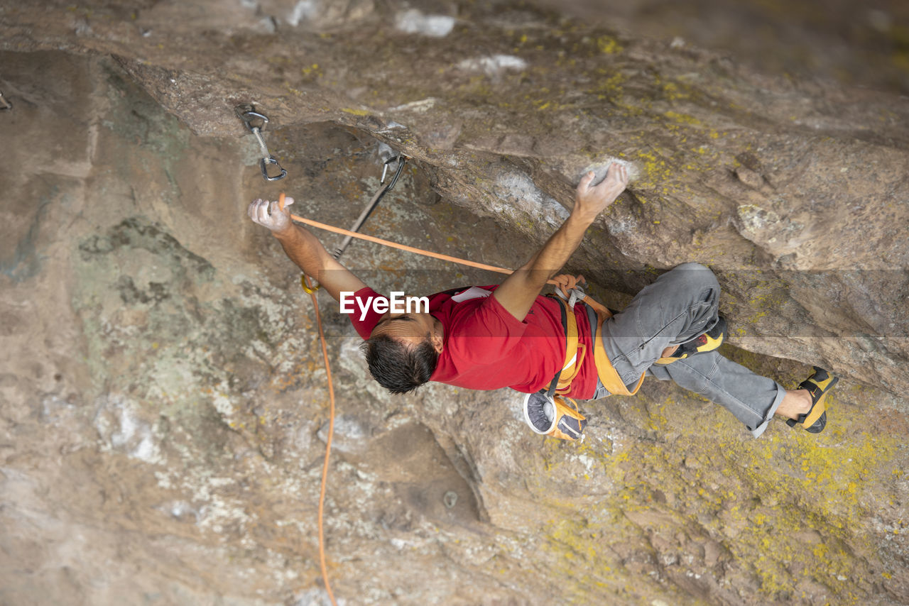 One man wearing red clips a carabiner with a rope while rock climbing