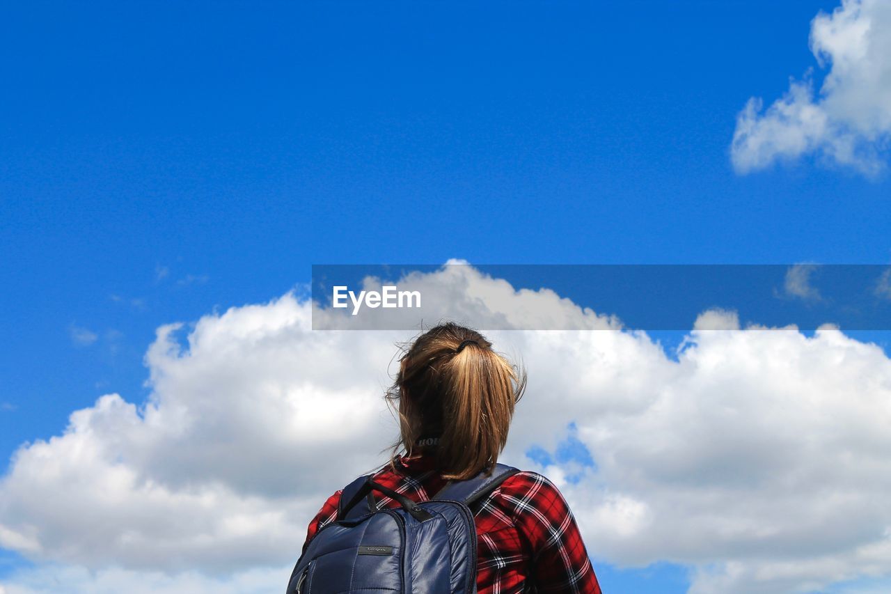 Rear view of backpack woman standing against blue sky