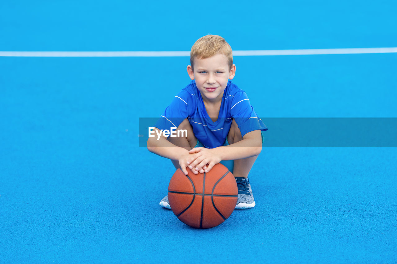 Portrait of boy holding basketball while crouching on court