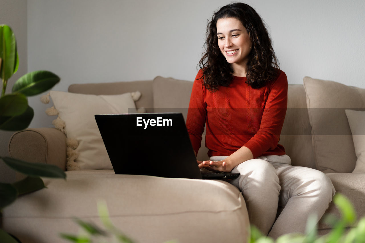 portrait of young woman using laptop while sitting on sofa at home