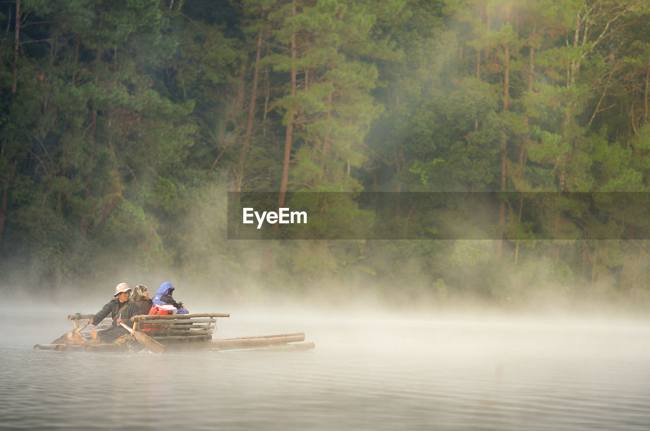 People on wooden raft in river against trees