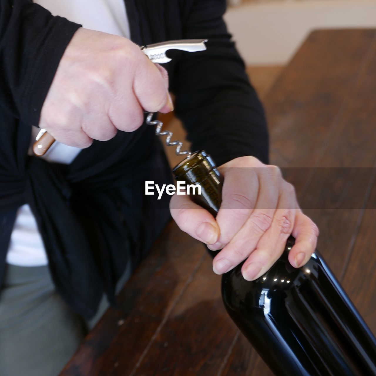 Midsection of man pulling cork from wine bottle