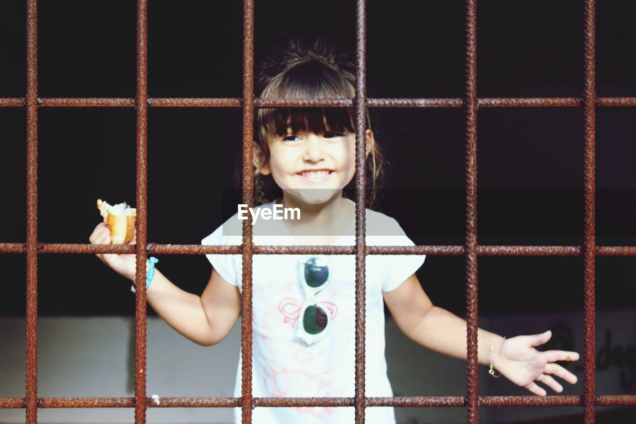 Happy girl holding food seen through metal grate