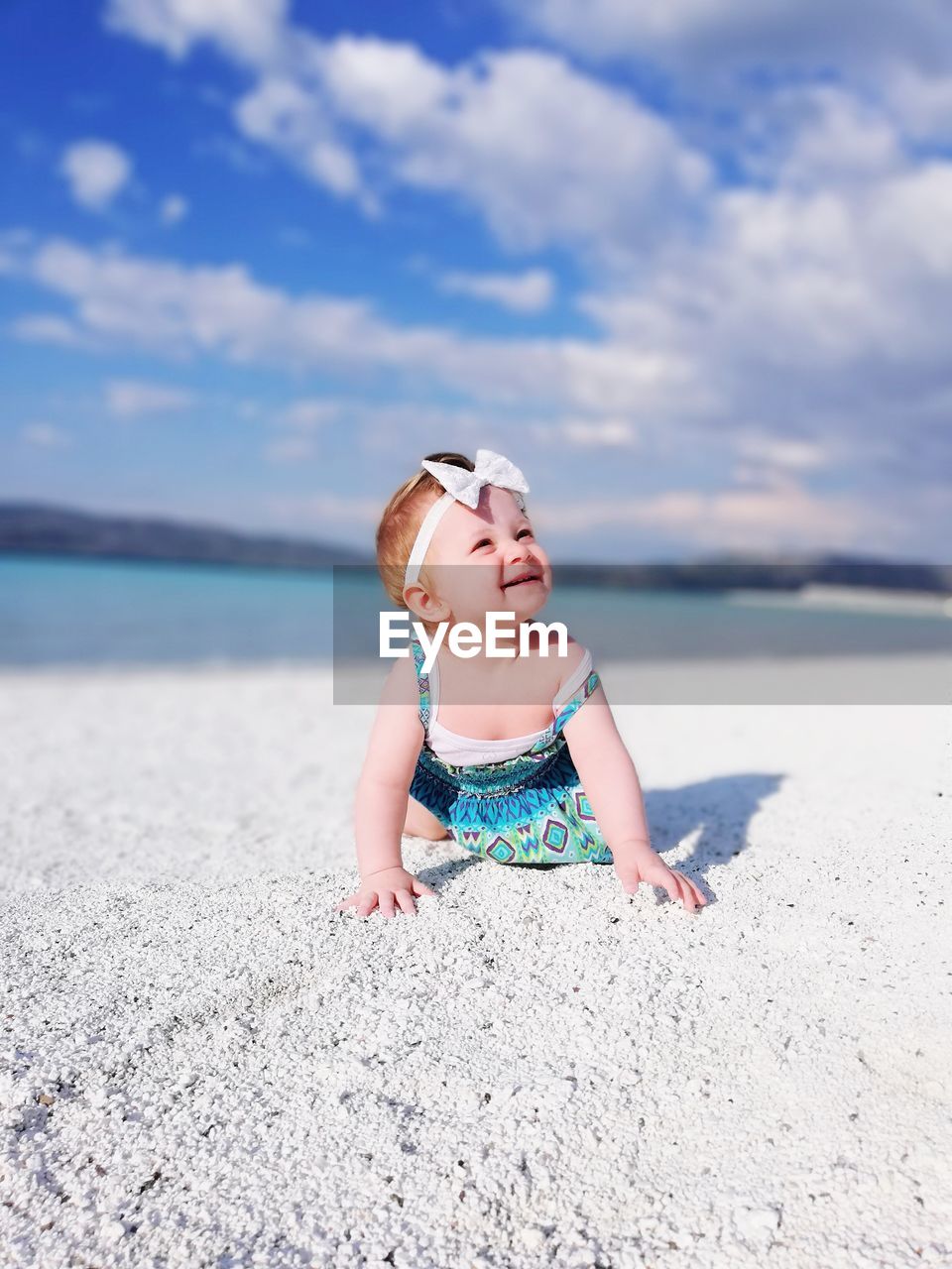 Baby girl crawling at beach against sky
