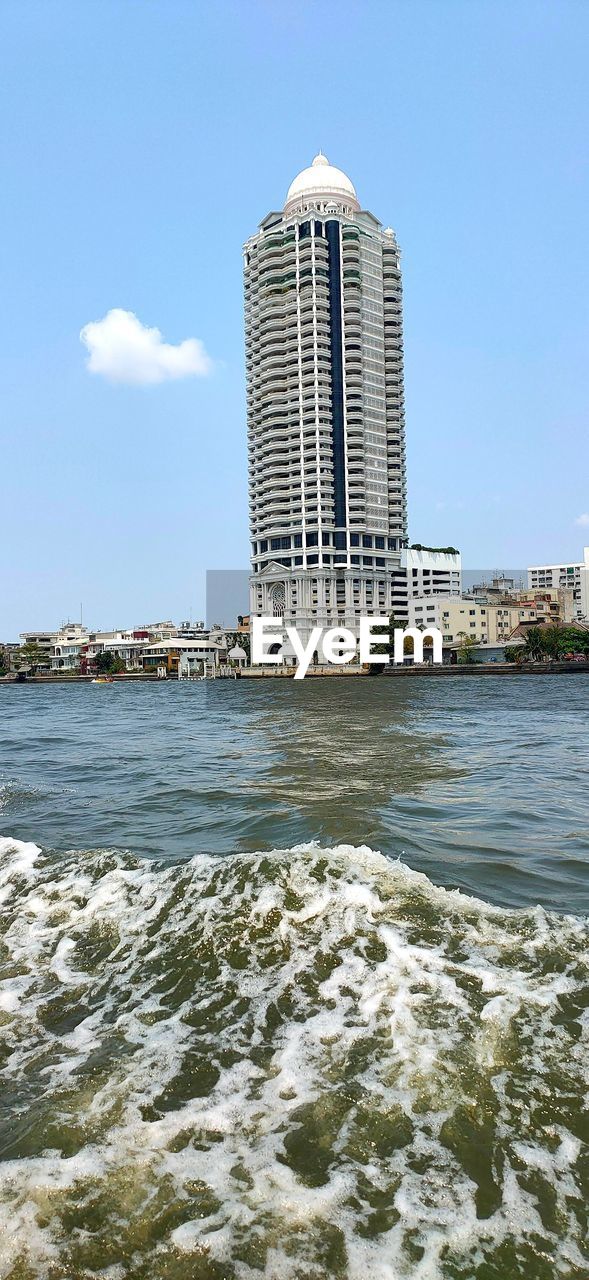 SEA BY MODERN BUILDINGS AGAINST SKY