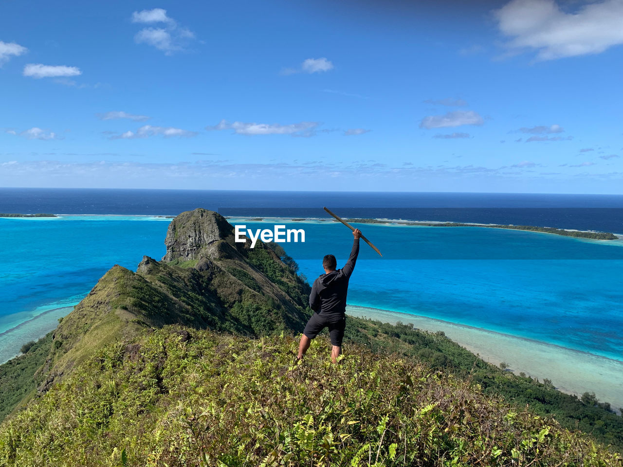 Rear view of man with hand raised standing on cliff by sea