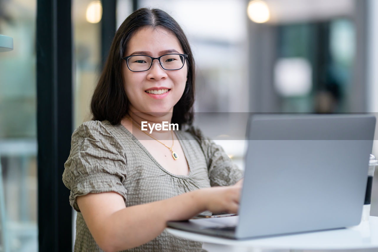 Portrait of smiling woman using laptop at cafe