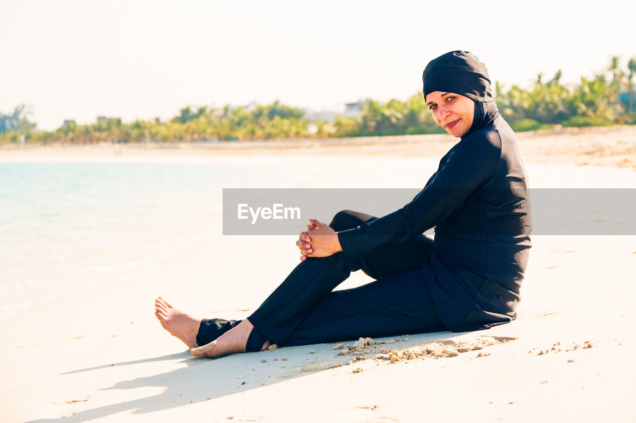 Portrait of smiling woman on beach against clear sky