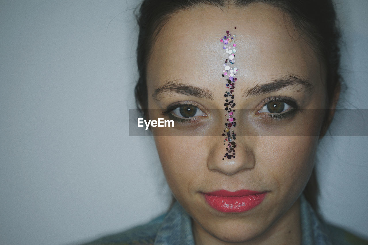 Portrait of beautiful young woman with sequins on face against wall