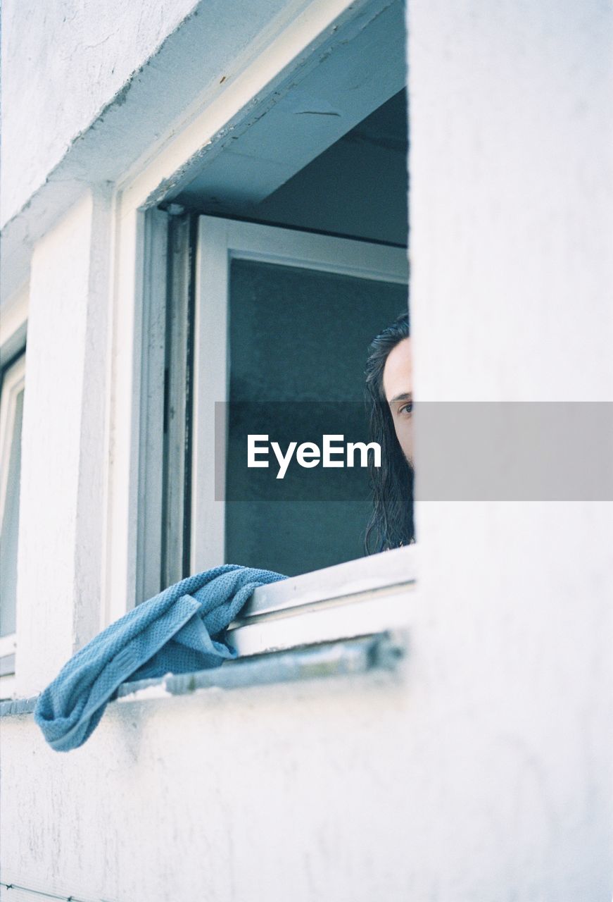 Portrait of young man looking through building window