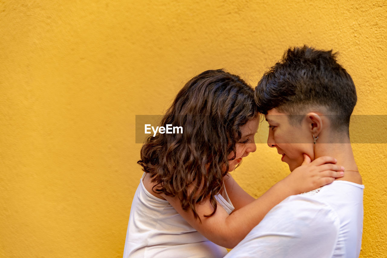 Side view of couple kissing against orange wall