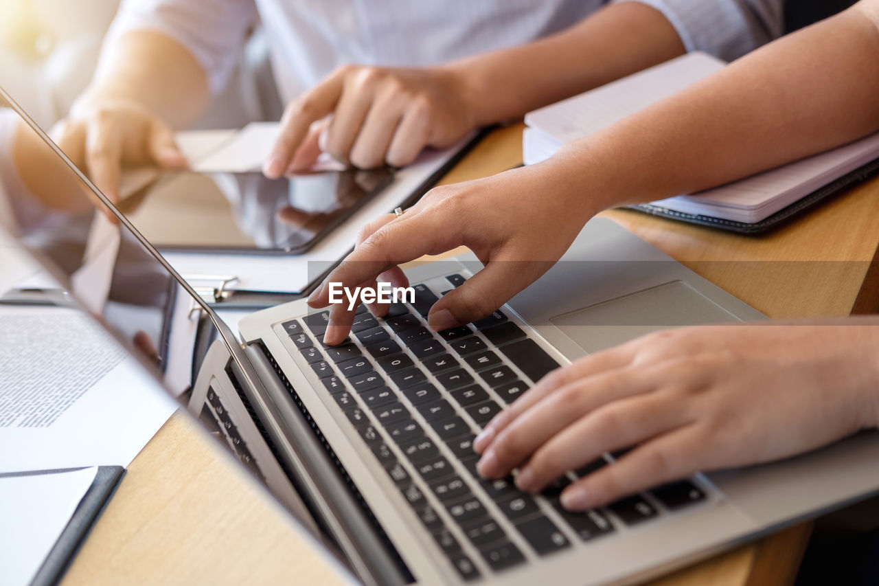 Midsection of colleagues using laptop and digital tablet on office desk