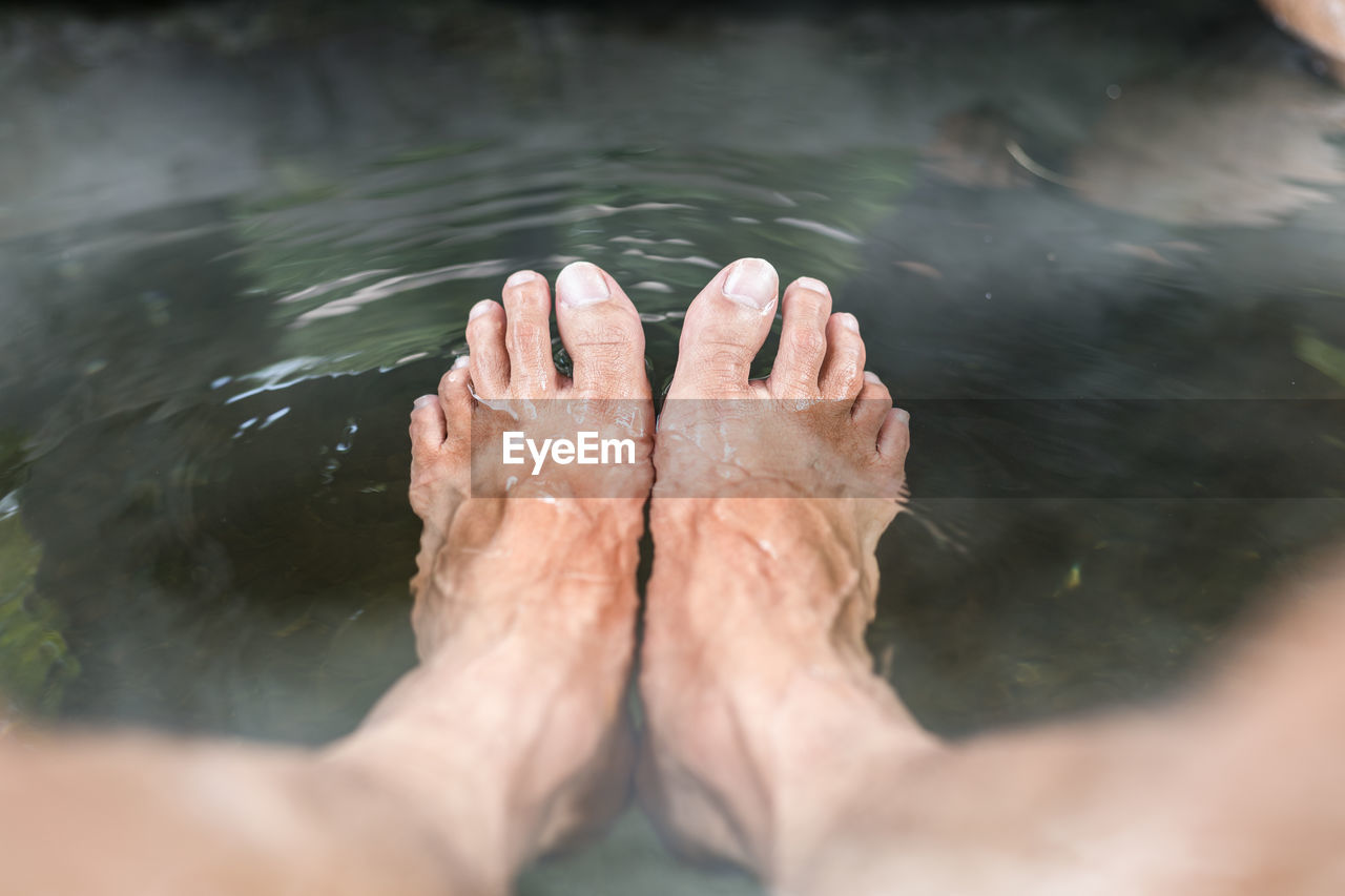 Low section of person relaxing in hot water spring lake