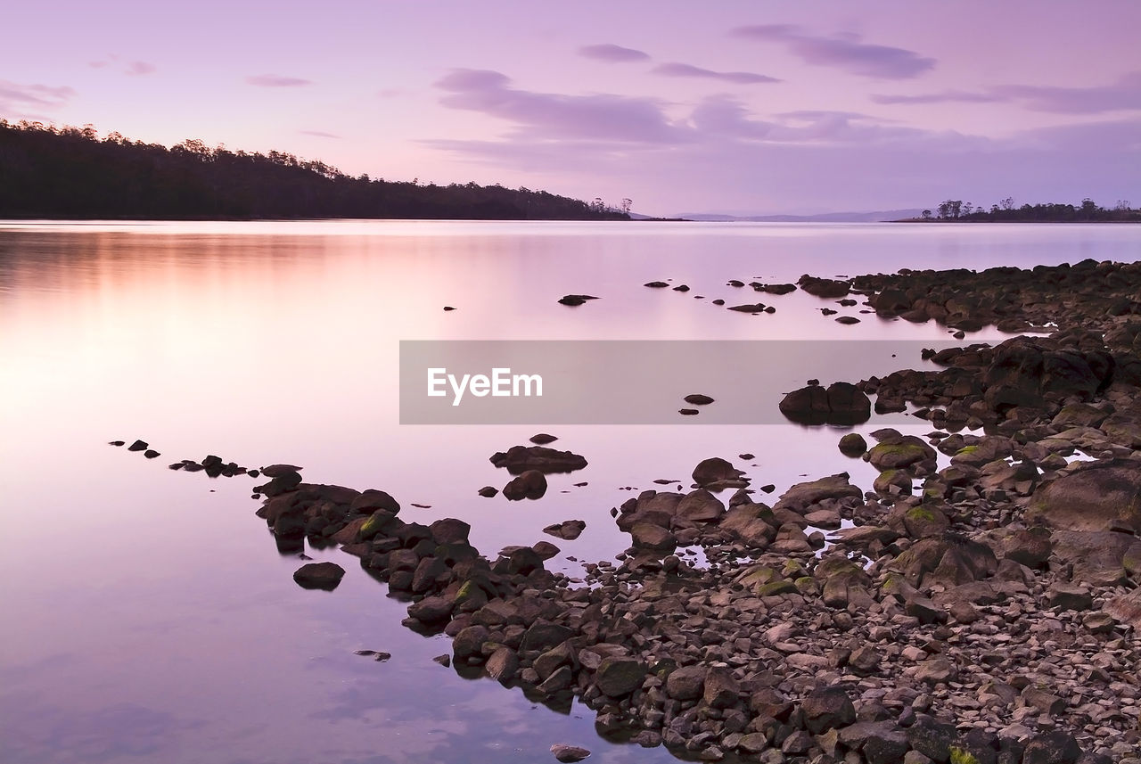 ROCKS BY LAKE AGAINST SKY DURING SUNSET