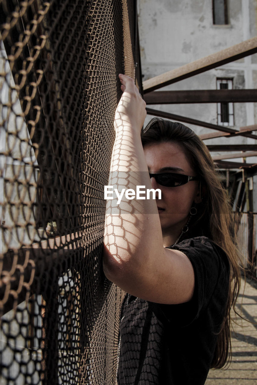 Young woman standing by metal fence