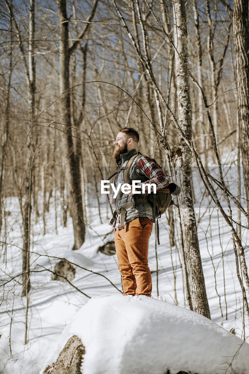 Man with beard wearing flannel stands on snow covered rock