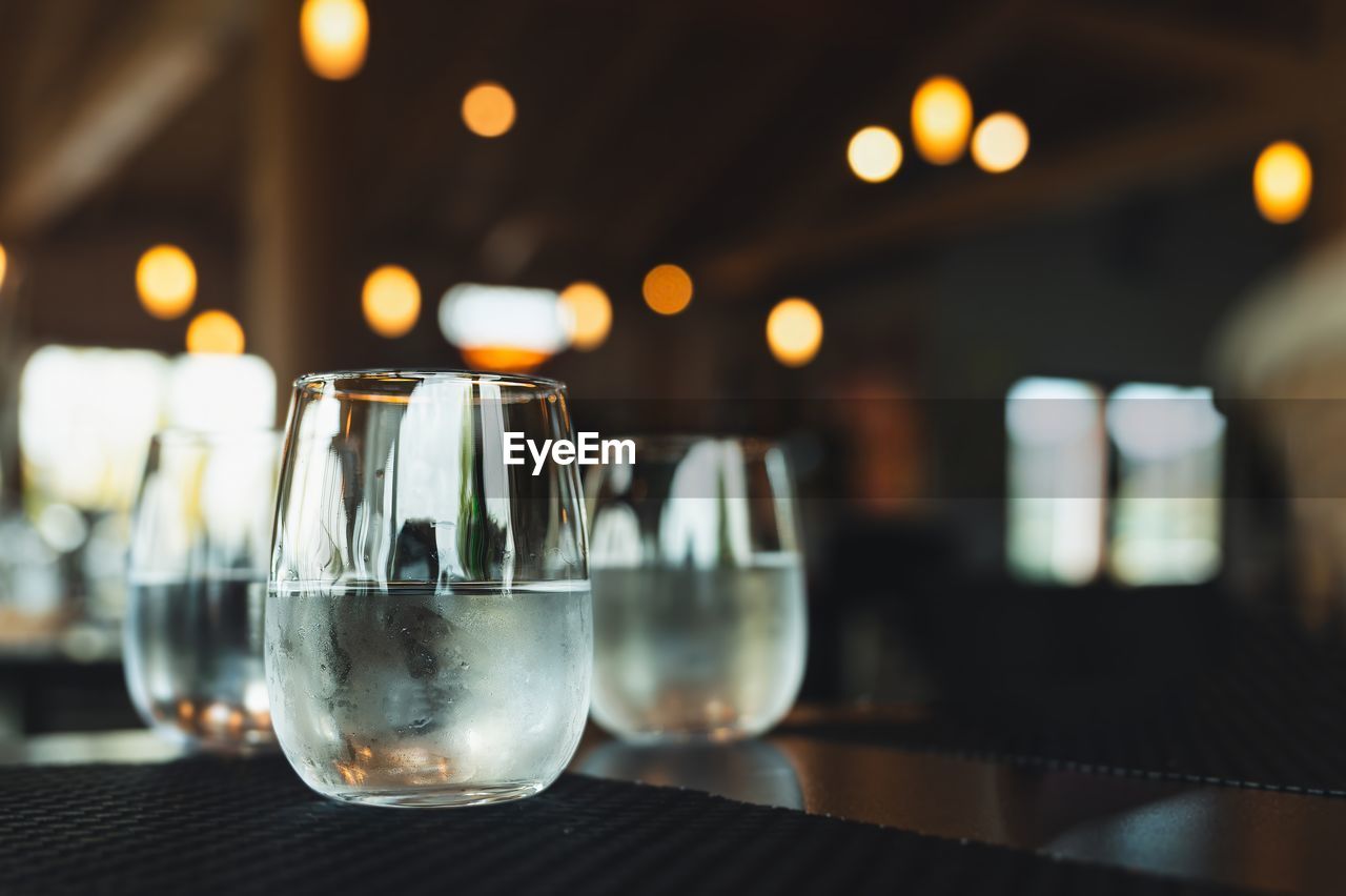 food and drink, glass, refreshment, drink, drinking glass, alcohol, table, household equipment, restaurant, focus on foreground, wine glass, indoors, no people, bar, lighting, wine, business, night, illuminated, close-up, bar counter, still life, freshness, alcoholic beverage, light, selective focus