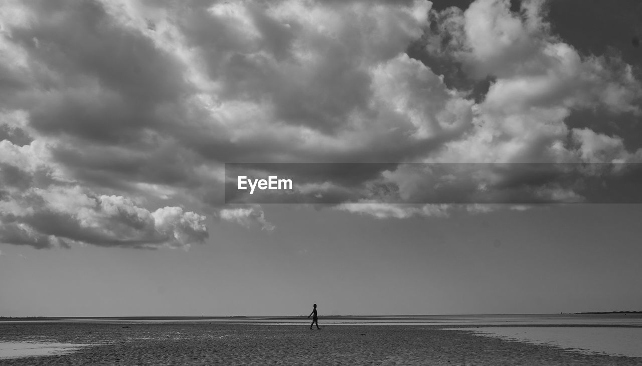 Scenic view of sea with person walking at beach against sky