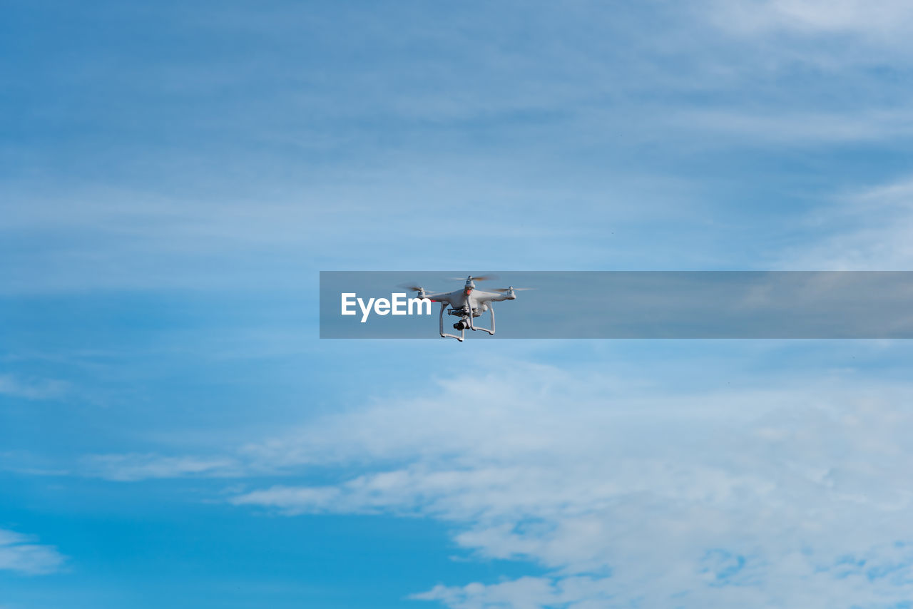 Low angle view of drone flying against blue sky during sunny day