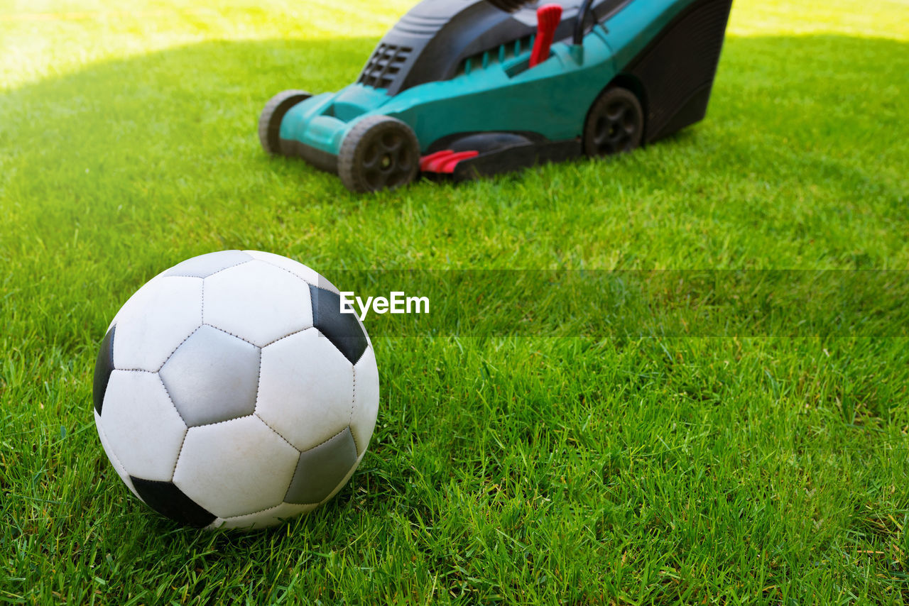 Soccer ball and lawn mower on a field in the grass. close-up. grass care