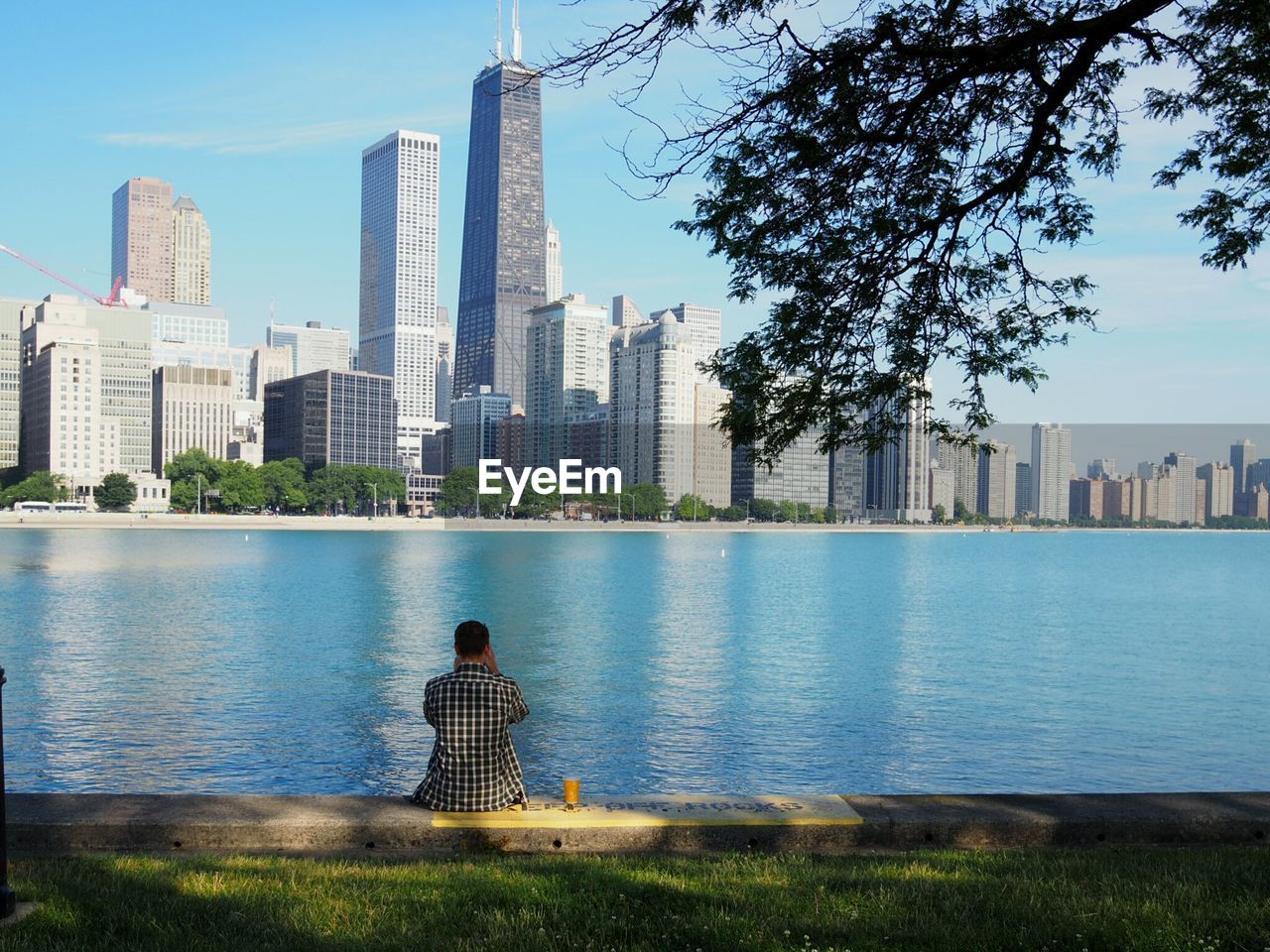 Rear view of man sitting by river against cityscape