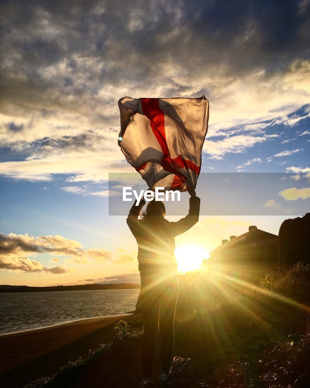Silhouette woman standing with english flag at beach against sky during sunset
