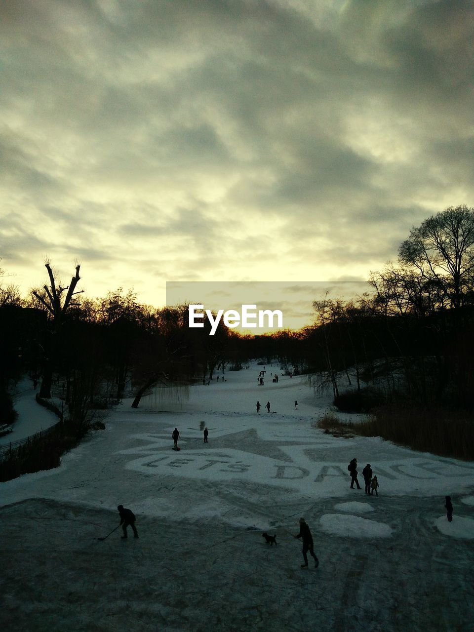 People at snow covered field against cloudy sky during sunset