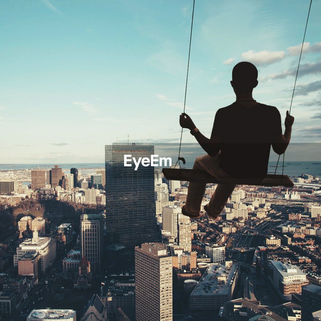 Rear view of man on swing against cityscape