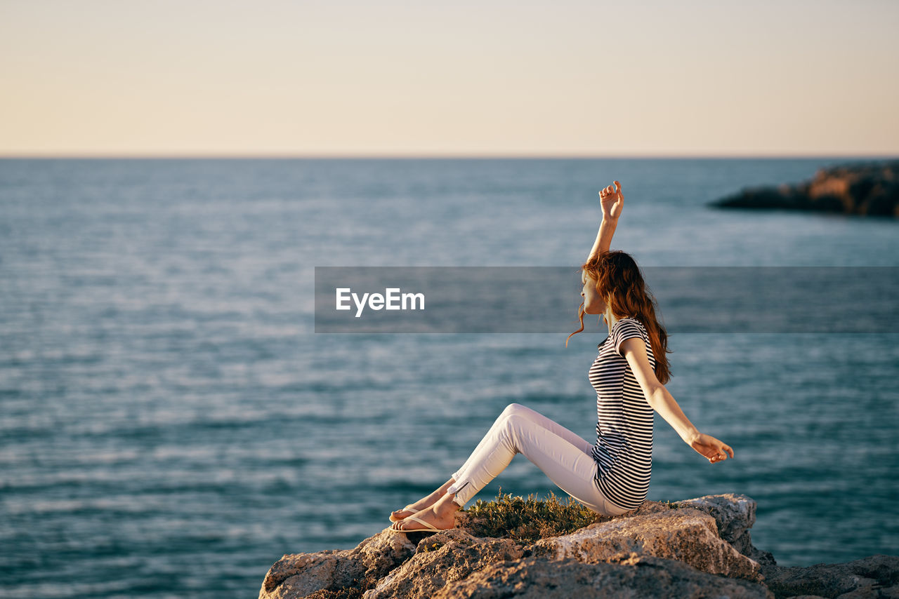 WOMAN STANDING ON ROCK AGAINST SEA