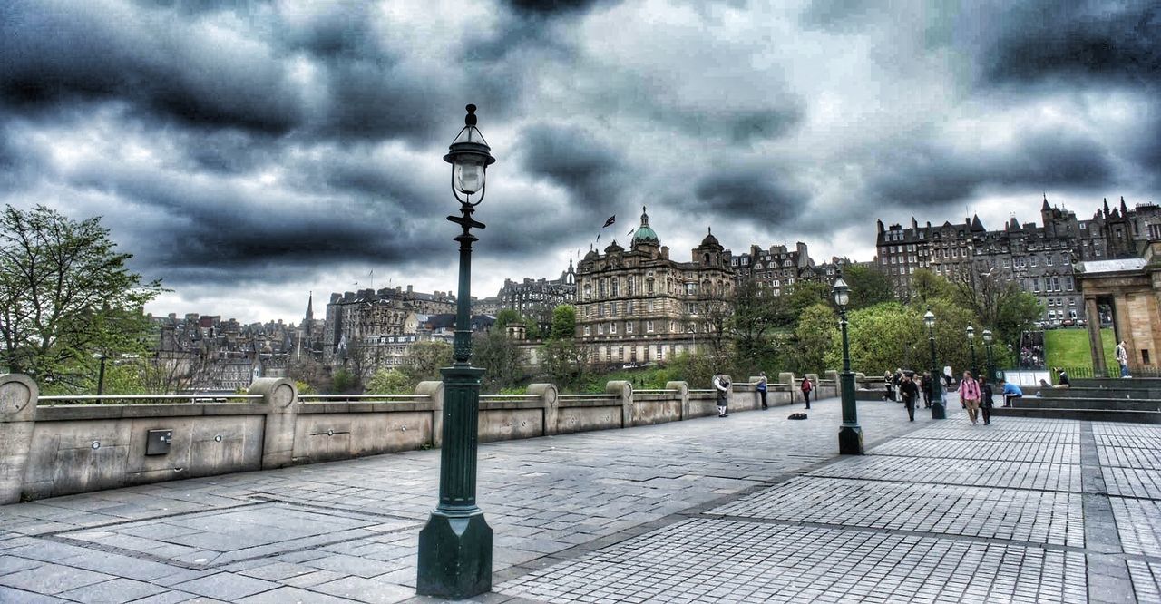 Street light on walkway against buildings and cloudy sky