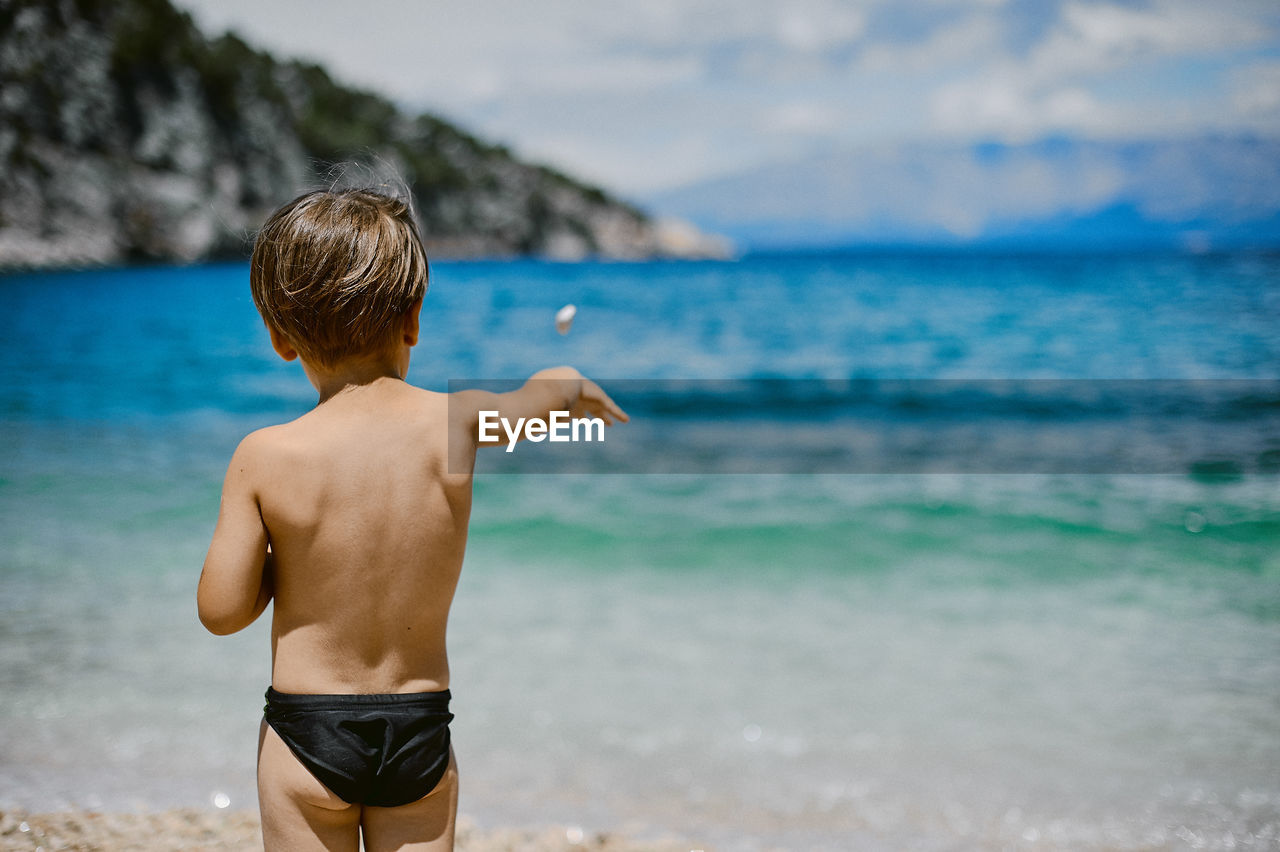 Rear view of shirtless boy standing at beach