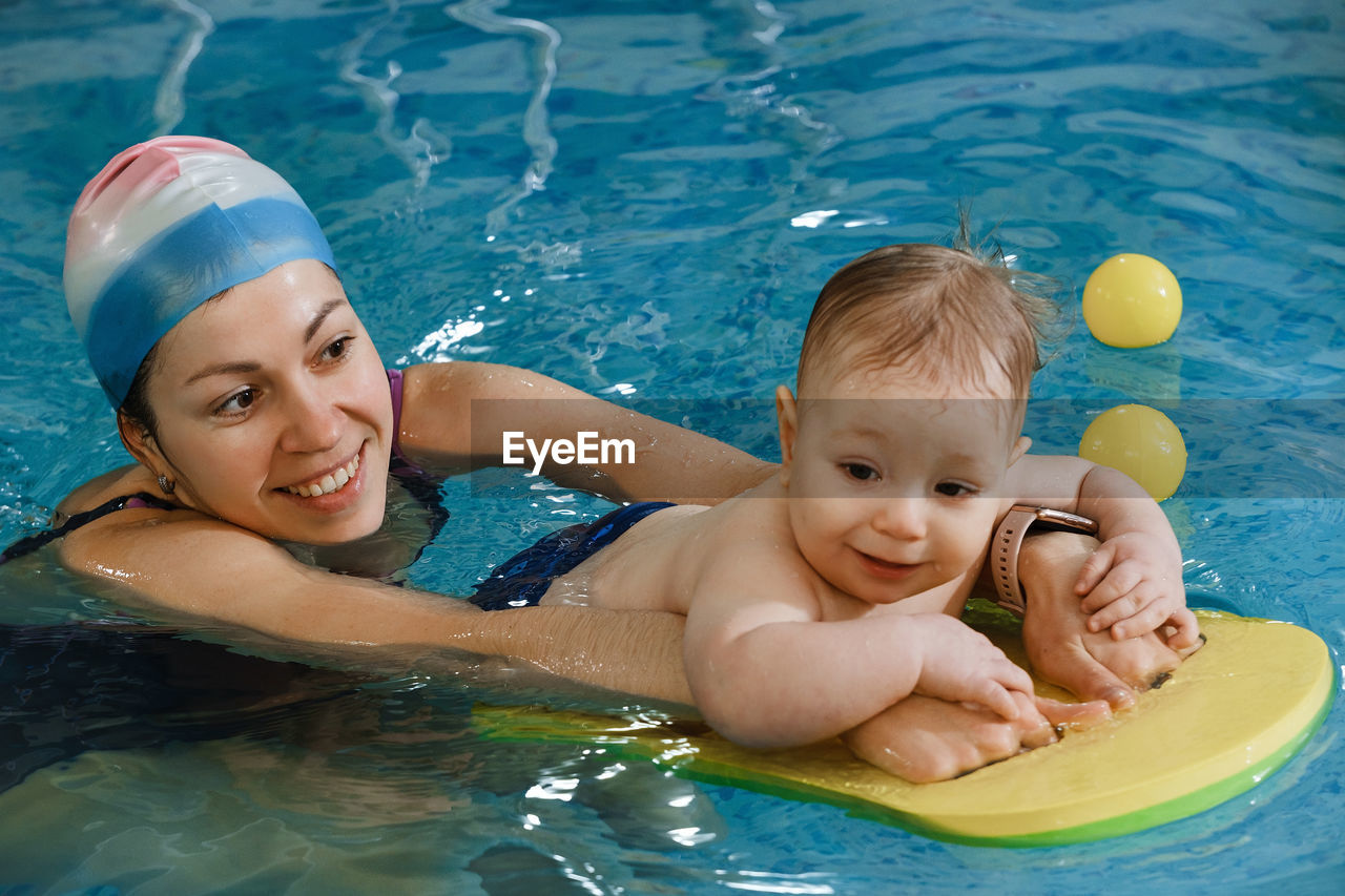 Early age swimming in pool. baby boy trained to swim in water coach woman in indoor swimming pool  