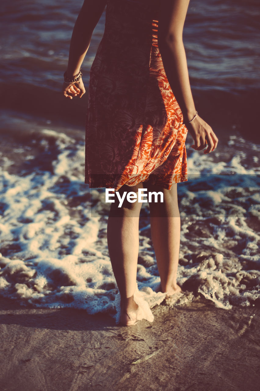 Low section of woman standing on shore at beach