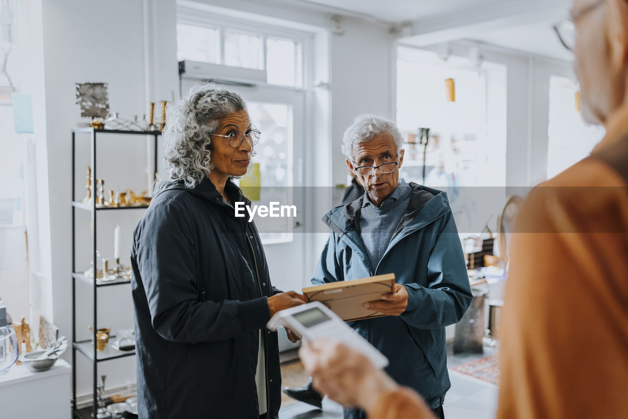 Senior couple buying picture frame and talking with salesman in antique shop