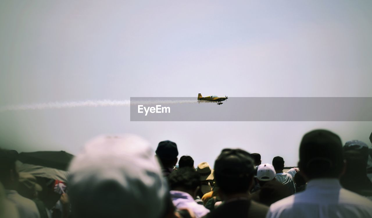 Rear view of people looking at airshow against sky